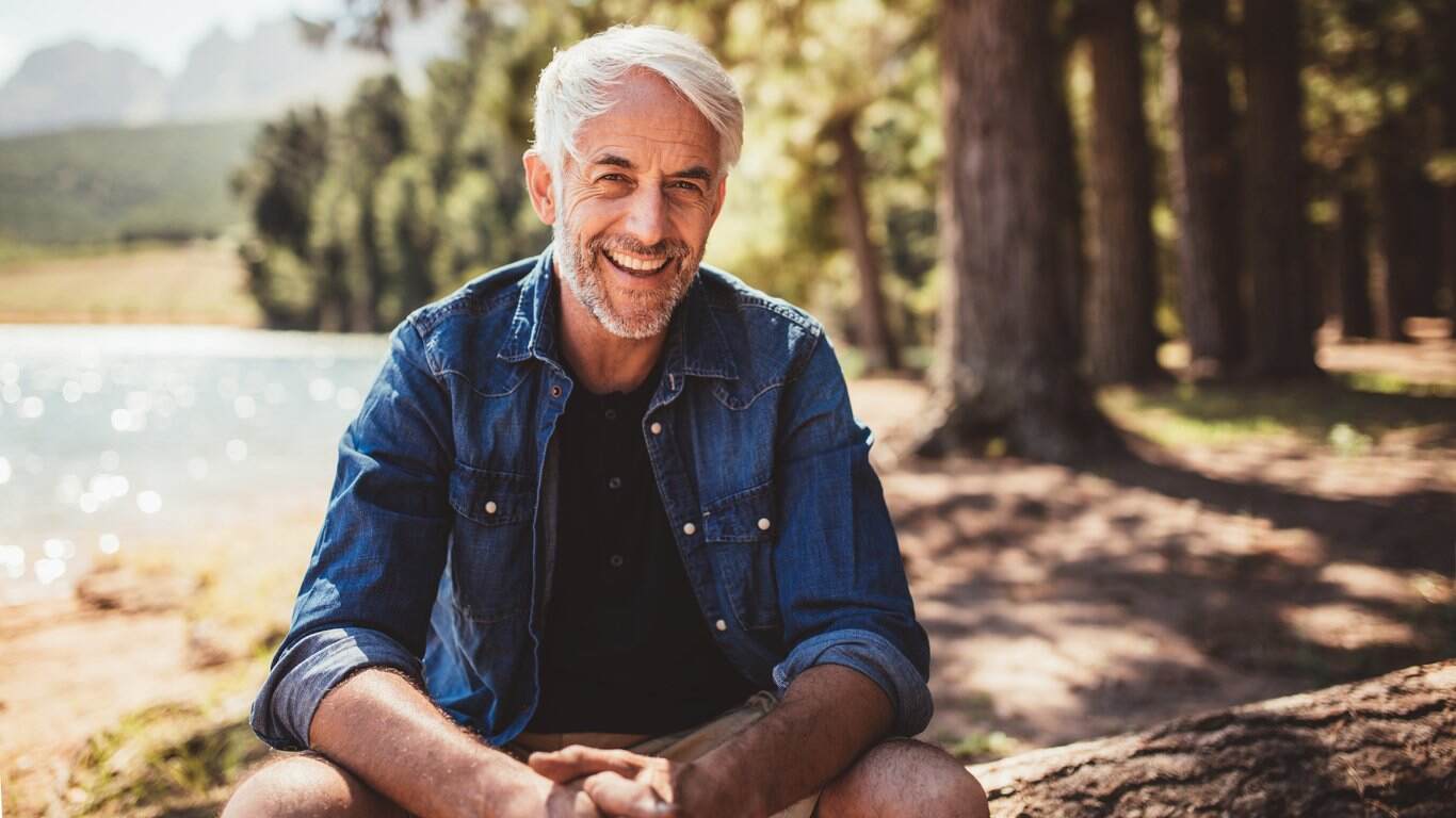 Happy mature man sitting near a lake